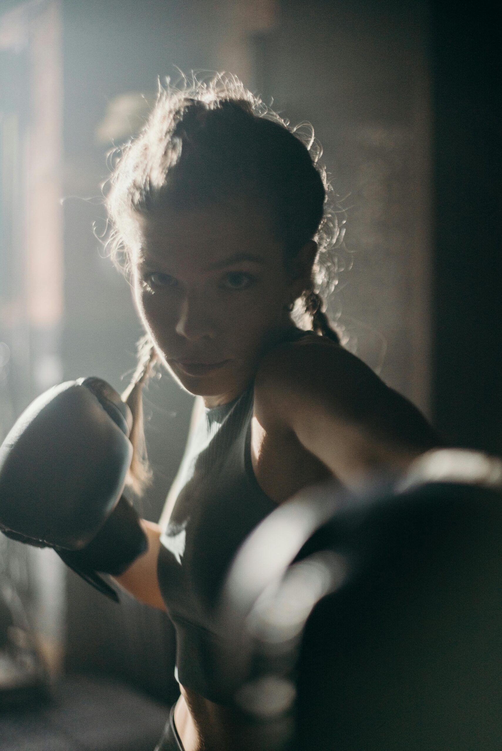 Focused female boxer in action, throwing a punch in a dimly lit gym.