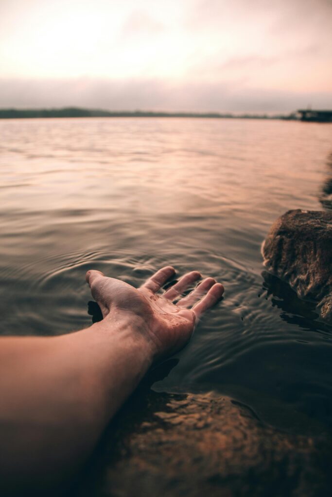 pexels-photo-2422560-2422560 A serene image of a hand touching the water at twilight, creating gentle ripples.